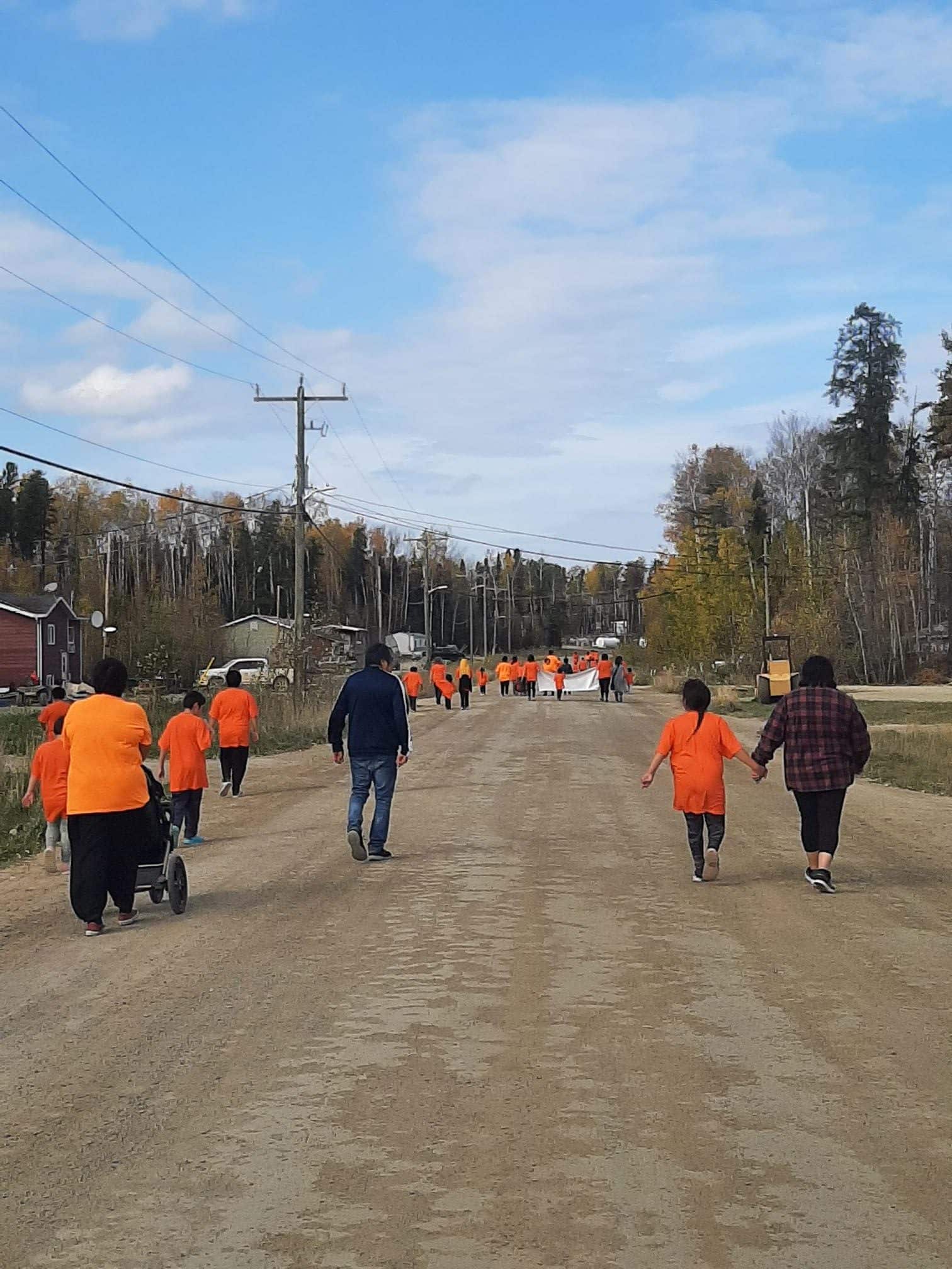A group of people in orange shirts walking down a dirt road.
